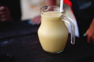 Delicious and healthy fruit shake served in a glass pitcher on a black surface.