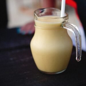 Delicious and healthy fruit shake served in a glass pitcher on a black surface.